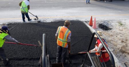 Strassenbauarbeiter verlegen Asphalt auf einer Strasse waehrend des Tages